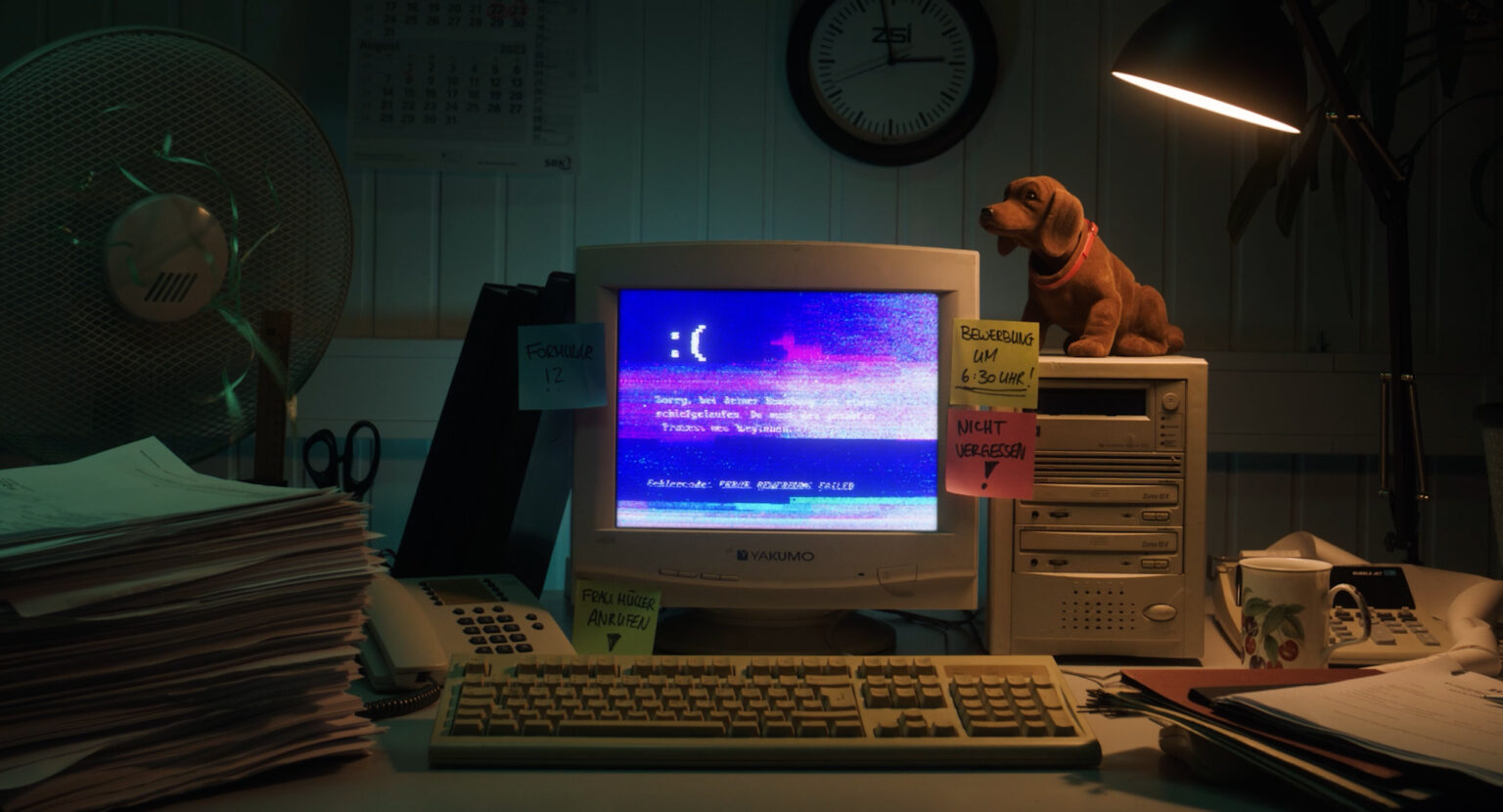 Standbild aus einer Werbung, die einen 90er-Jahre-Computer mit Bluescreen in einer Retro-Büroatmosphäre zeigt.