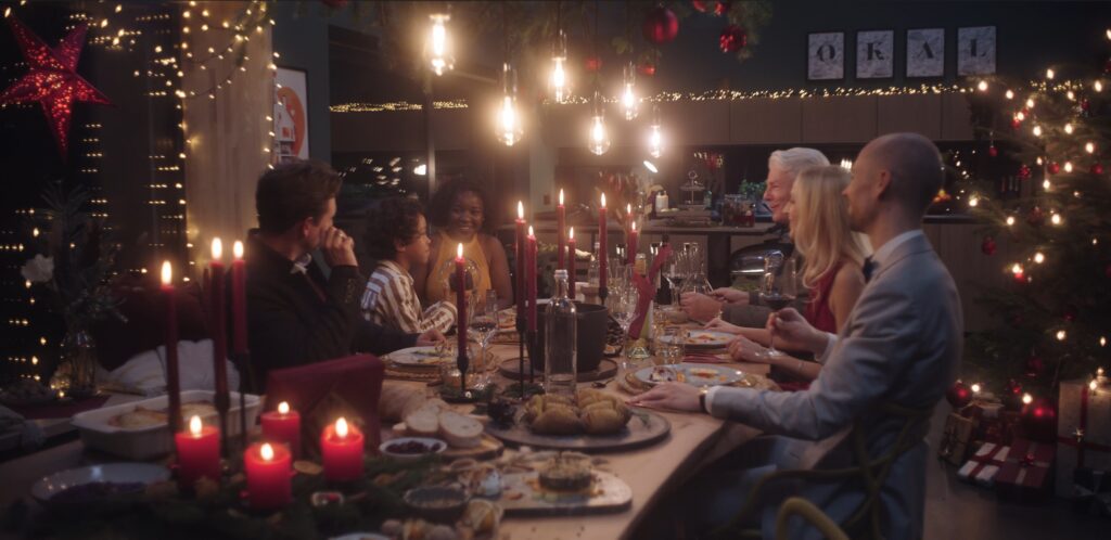 OKAL Herz des Hauses Thumbnail, eine glückliche Familie die gemeinsam an einem reichlich gedeckten Weihnachtstisch sitzen.